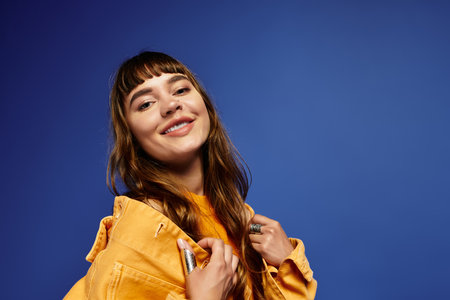 A trendy young woman shows off her style while smiling against a deep blue background.
