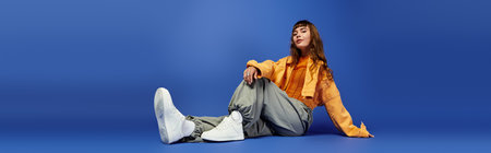 A chic young woman sits casually in trendy clothing, exuding confidence and style in a blue setting.