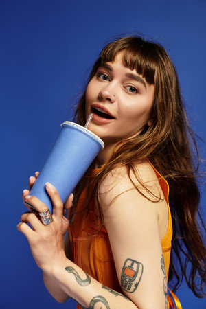 A young woman with fashionable attire playfully holds a drink, radiating joy and confidence.の写真素材