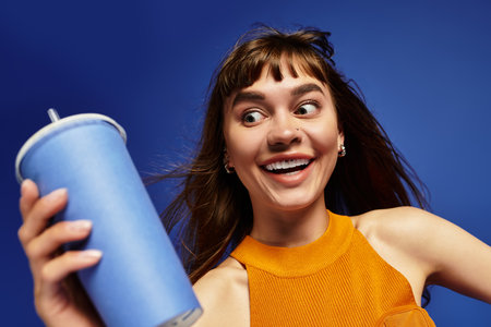 A young fashionable woman joyfully holds a drink, showcasing her stylish outfit and vibrant energy.