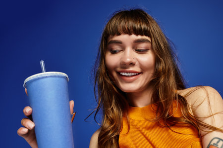 Chic woman in fashionable attire smiles while holding a colorful beverage in vibrant setting.