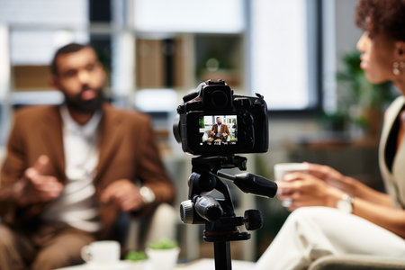A woman interviews a man in a sleek studio, capturing every moment with a camera.