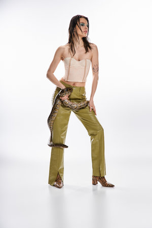A confident young woman showcases bold fashion while holding a snake in a studio.