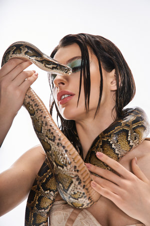A young, beautiful woman poses confidently with a snake wrapped around her arms.