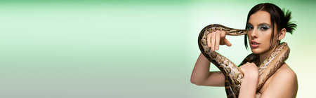 A young woman displays boldness with a snake around her neck, softly lit.