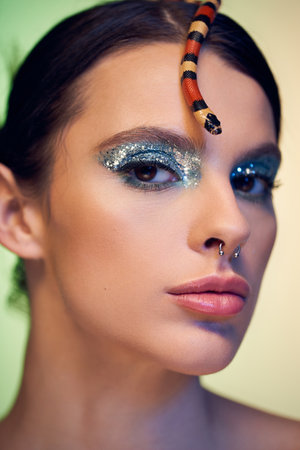 Young woman elegantly poses with a snake on her head, flaunting vibrant makeup and confidence.