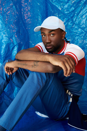 A handsome young man sits thoughtfully on the floor in striking blue attire.