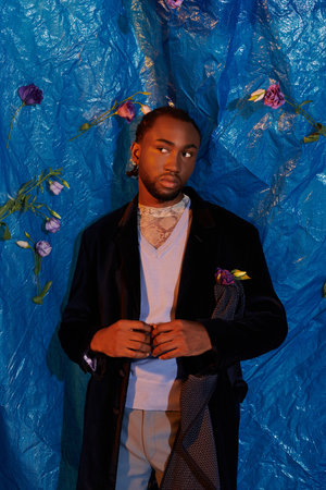 A stylish young man stands confidently in front of a blue backdrop, showcasing elegance and charm.の写真素材