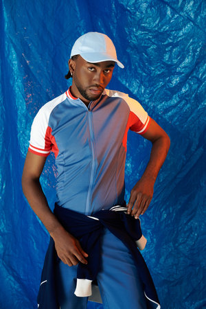 A stylish young man stands confidently against a striking blue backdrop.