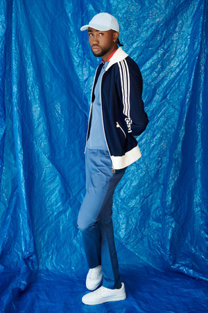 A young man confidently displays his stylish outfit against a bold blue backdrop.