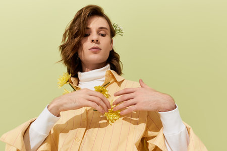 Handsome man in stylish outfit poses gracefully against a pastel backdrop, adorned with flowers.