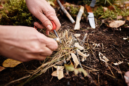 A senior woman is skillfully starting a fire using dry grass and twigs in the forest.の写真素材