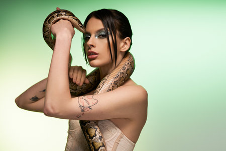 A young woman holds a snake elegantly around her neck, radiating beauty in soft light.の写真素材
