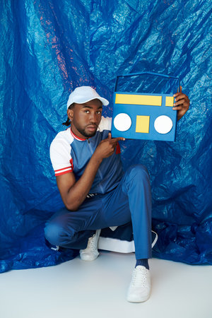 Handsome young man showcases vintage boombox while dressed casually against a bright blue backdrop.