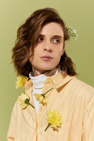 A stylish young man wears flowers in his hair against a calming green backdrop.