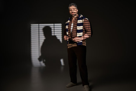 A fashionable man with bristle poses confidently in a modern studio, showcasing his trendy outfit.