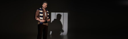 A confident man showcases his trendy outfit in a stylish studio, illuminated by striking lighting,...