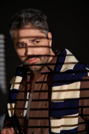 A handsome man with bristle poses confidently in a trendy outfit amidst studio lighting.の写真素材