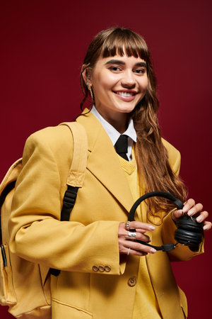 A young female student smiles brightly, dressed in a yellow ensemble with headphones in hand.の写真素材