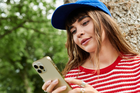 A beautiful female student reads on her phone, relaxed and content in a vibrant outdoor setting.