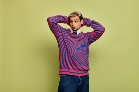 A stylish young man confidently poses in a unique striped sweatshirt amidst green hues.