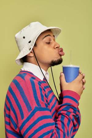 A fashionable young man is playfully sipping from a drink, dressed in a vibrant striped sweatshirt.の写真素材
