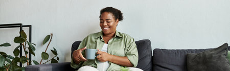 Relaxing in her modern apartment, a woman enjoys her drink while sitting on a comfortable sofa,...