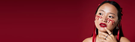 Young woman showcases unique makeup with bold bows on her cheeks in a studio setting, bannerの写真素材