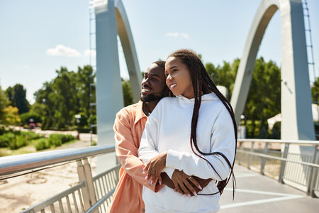 Loving couple embraces each other on a beautiful sunny day while walking on a bridge in the park.