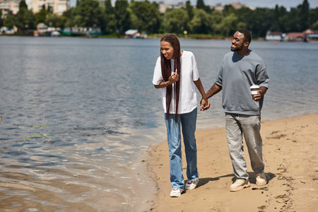 Loving couple walks hand in hand along the sandy lakeside, sharing smiles and laughter together.の写真素材