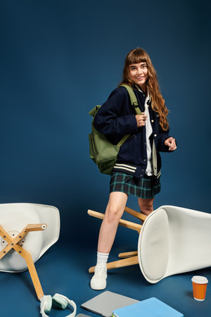 Cheerful young woman in bright clothes poses playfully among overturned chairs and books.