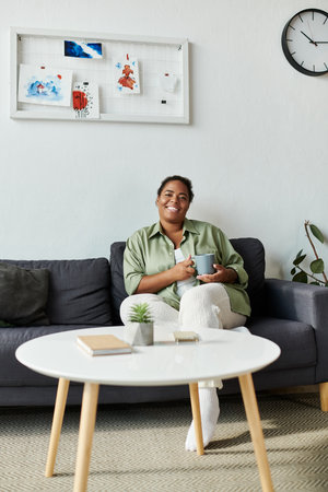 An African American woman enjoys her cozy home, relaxing with a warm drink in her hands.の写真素材