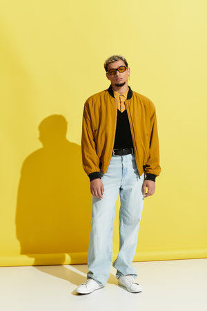 Stylish young man un sunglasses showcasing the latest fashion trends in a yellow studio setting.