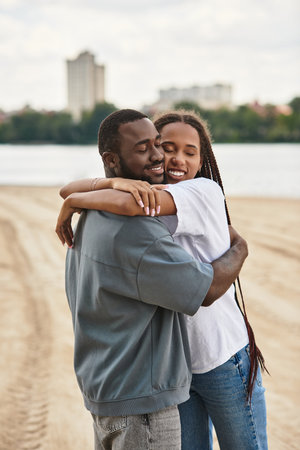 Loving couple shares a warm hug outdoors while exploring the riverside together.の写真素材
