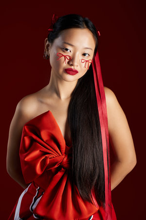 A young Asian woman showcases bold creativity with innovative makeup and vibrant red details.の写真素材
