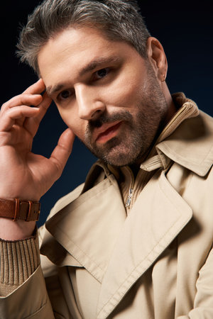 A confident man poses in a trendy trench coat, highlighting contemporary style in a studio setting.の写真素材