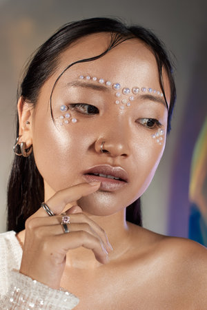 Young woman showcases creative makeup with pearls on her face, exuding beauty and artistry.の写真素材