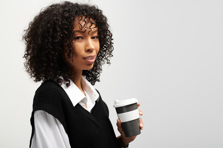 A young woman in business attire stands confidently, sipping coffee on her break.の写真素材