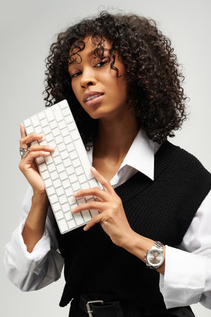 Elegant young woman poses with a keyboard while showcasing her stylish business attire.の写真素材