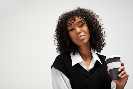 A confident woman with curly hair holds a coffee cup while showcasing her elegant business attire.の写真素材