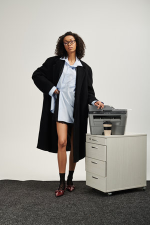 A young woman in a chic outfit exudes elegance next to a sleek office printer.