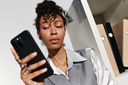 Confident young woman in elegant attire focuses on her smartphone in a chic office.の写真素材