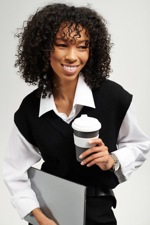 Bright smile radiates confidence as the young woman holds a coffee cup and tablet, embodying grace.の写真素材