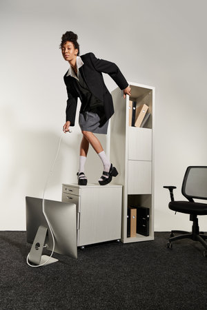 A young woman stands confidently on a filing cabinet, showcasing her elegant business attire.