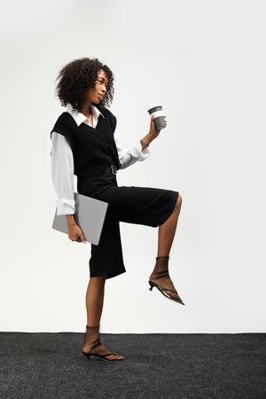 Young beautiful woman exudes elegance in business attire while confidently holding a coffee cup.の写真素材
