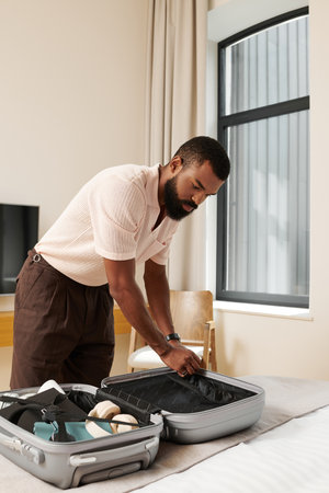 Setting a suitcase in a stylish hotel room, a man organizes his vacation essentials with care.の写真素材