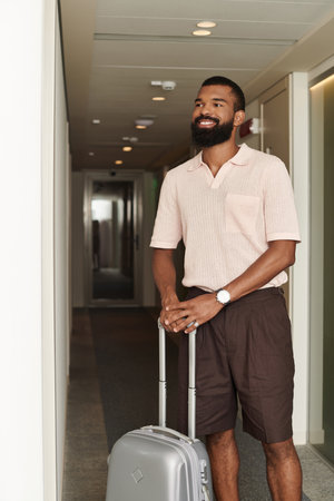 A stylish African American man standing in a hall near modern hotel room, eager for adventure.の写真素材