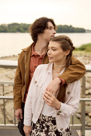 A young couple shares a tender moment as they stroll hand in hand by the water, radiating joy.の写真素材