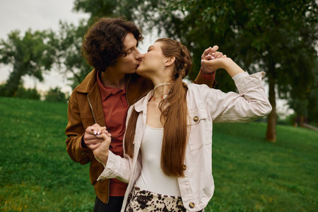 A young couple shares a sweet kiss while strolling through a peaceful park, radiating love and joy.の写真素材