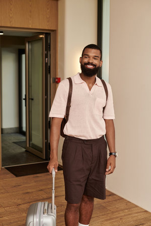 A stylish African American man with a suitcase smiles as he enters a contemporary hotel lobby.の写真素材